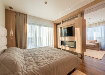 Interior of spacious apartment with cozy living room with soft bed separating from living room with sliding doors and wall with TV set in sunlight